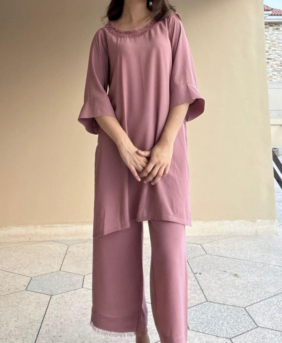 Person wearing a light pink outfit standing on a tiled floor with a neutral wall background