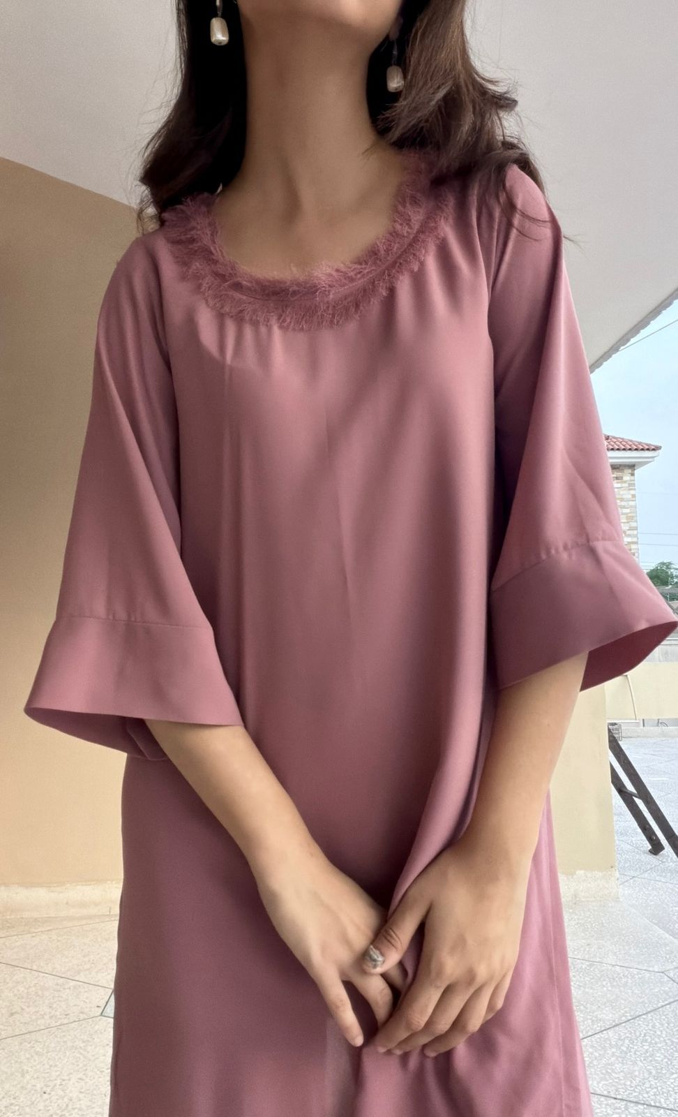 Woman wearing a light pink dress with lace neckline outdoors.