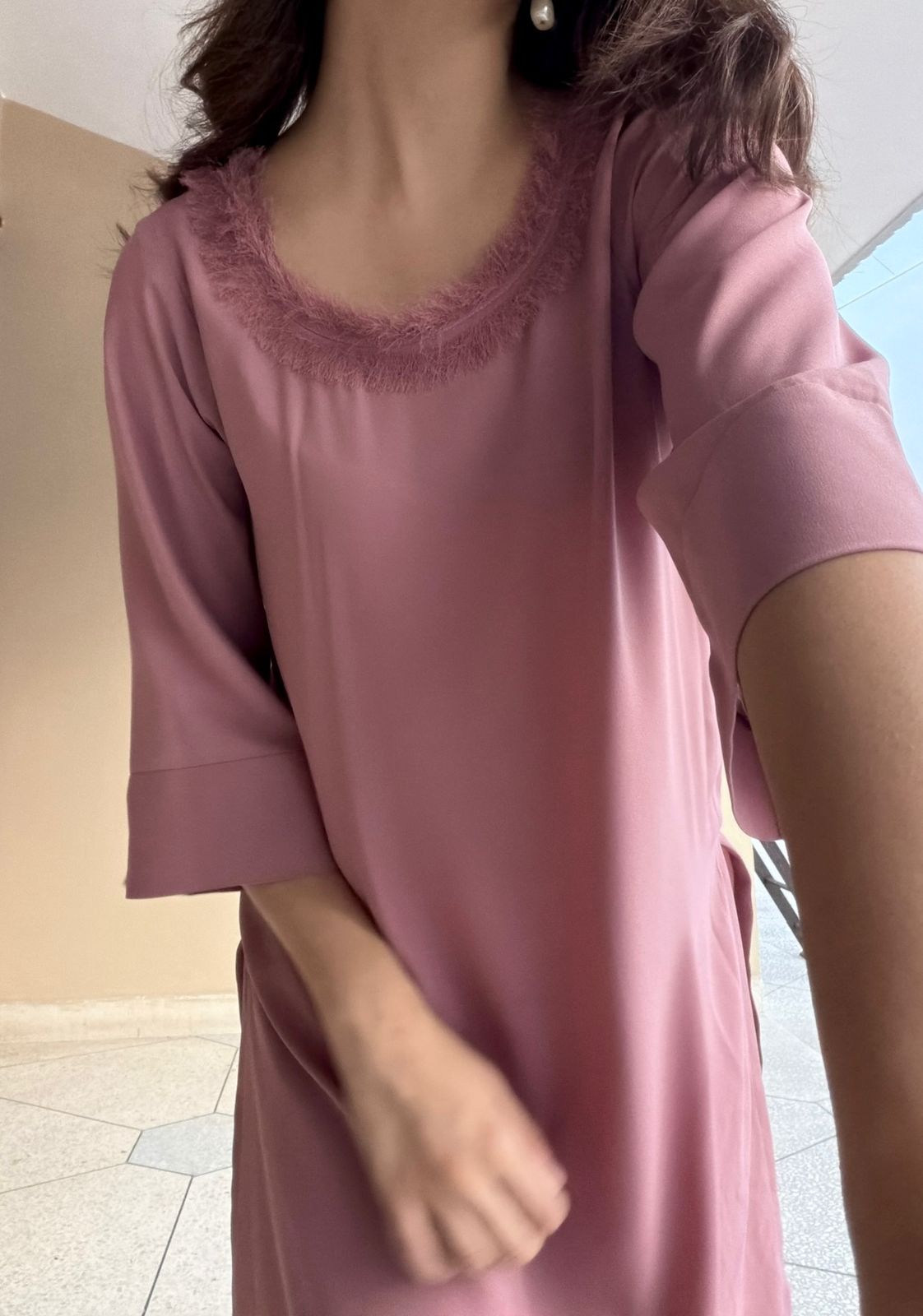 Person wearing a light pink dress with lace neckline indoors.