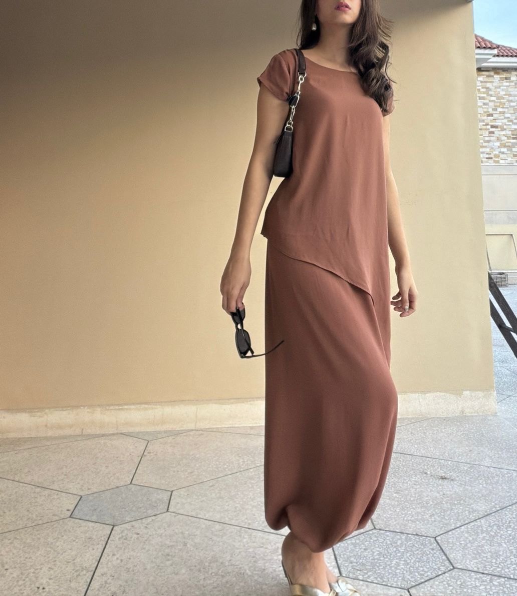 Woman wearing a brown outfit standing against a beige wall.