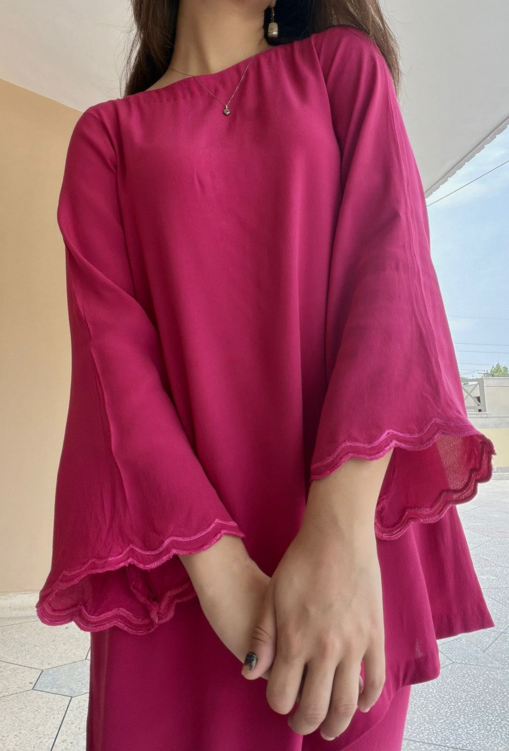 Person wearing a magenta dress with ruffled sleeves in an outdoor setting