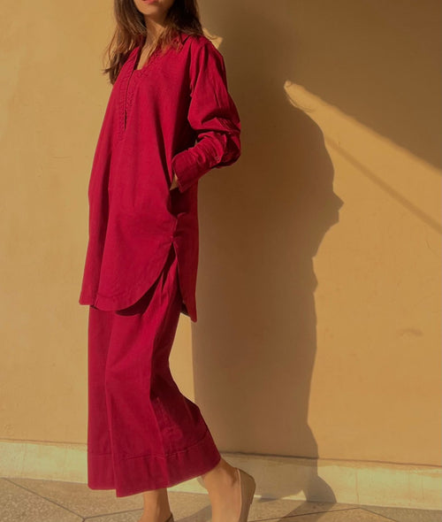 Person wearing a burgundy outfit standing against a beige wall.