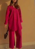Person wearing a burgundy outfit against a beige wall