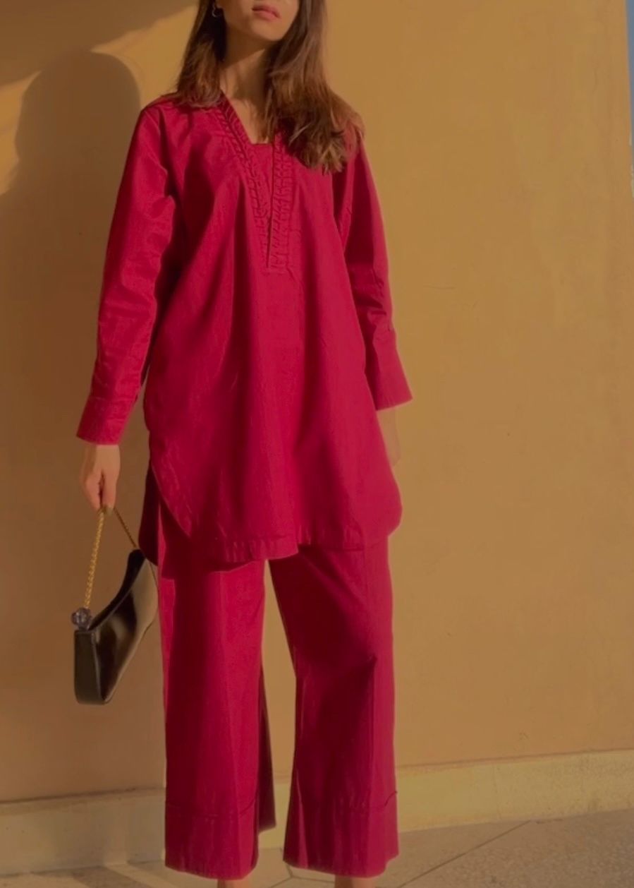 Person wearing a burgundy outfit against a beige wall
