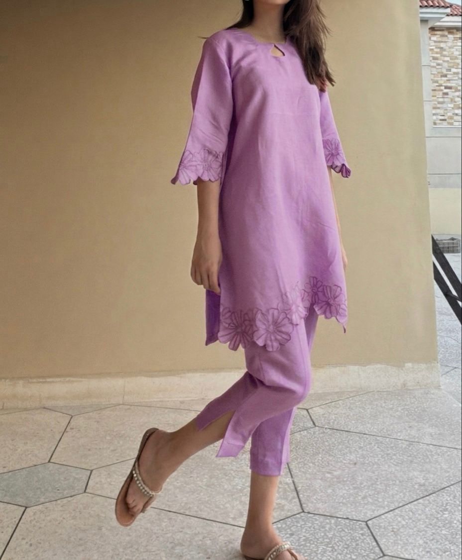 Person wearing a purple outfit with floral embroidery on a tiled floor.