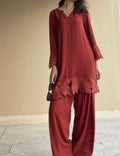 Person wearing a maroon outfit with lace details against a beige wall.