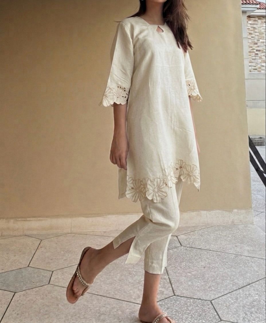 Woman wearing a white outfit with embroidery details on a beige wall background