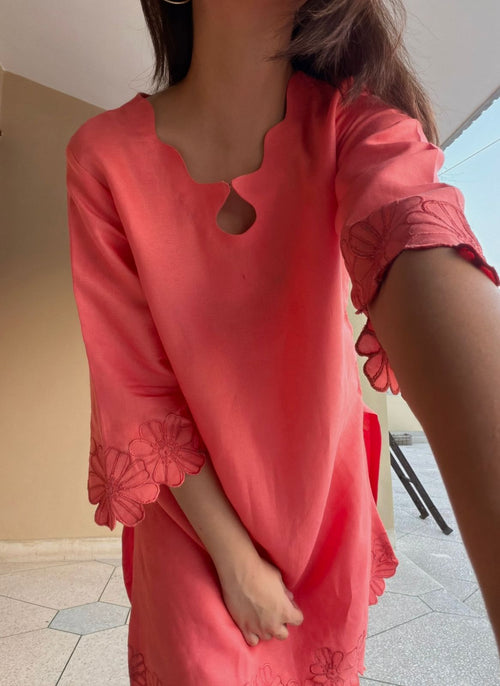 Person wearing a coral pink dress with floral details indoors.