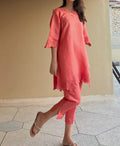 Woman wearing a coral dress with lace details on a tiled floor.