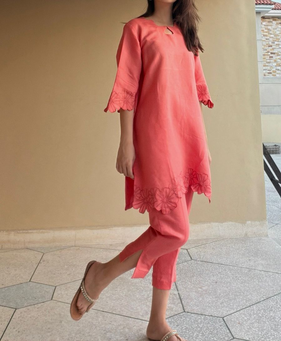 Woman wearing a coral dress with lace details on a tiled floor.